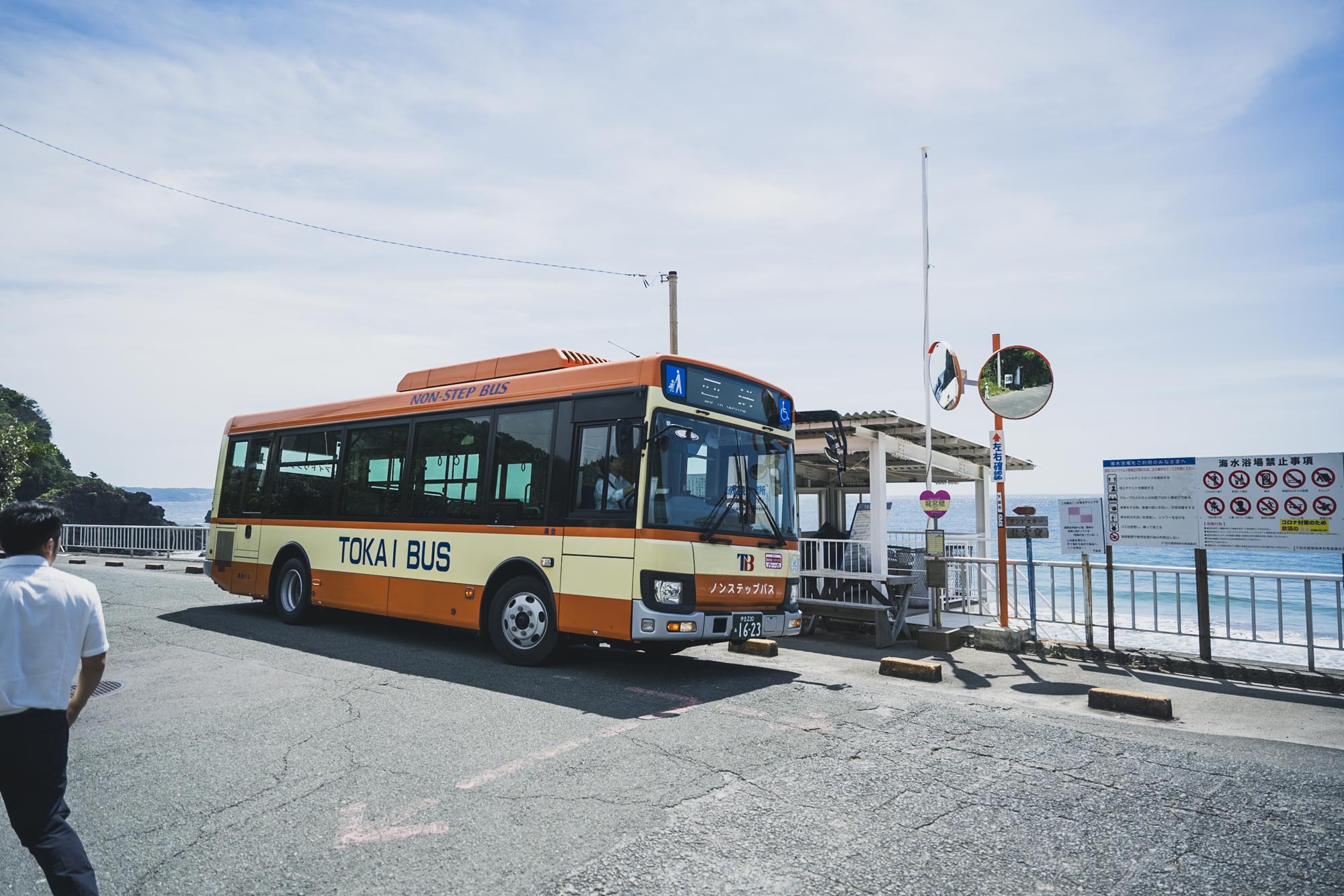 伊豆の青い海を背景に走る東海バスの路線バス。車体には温かみのあるカラーリングが施され、停留所で乗客を待つ穏やかな日常の風景