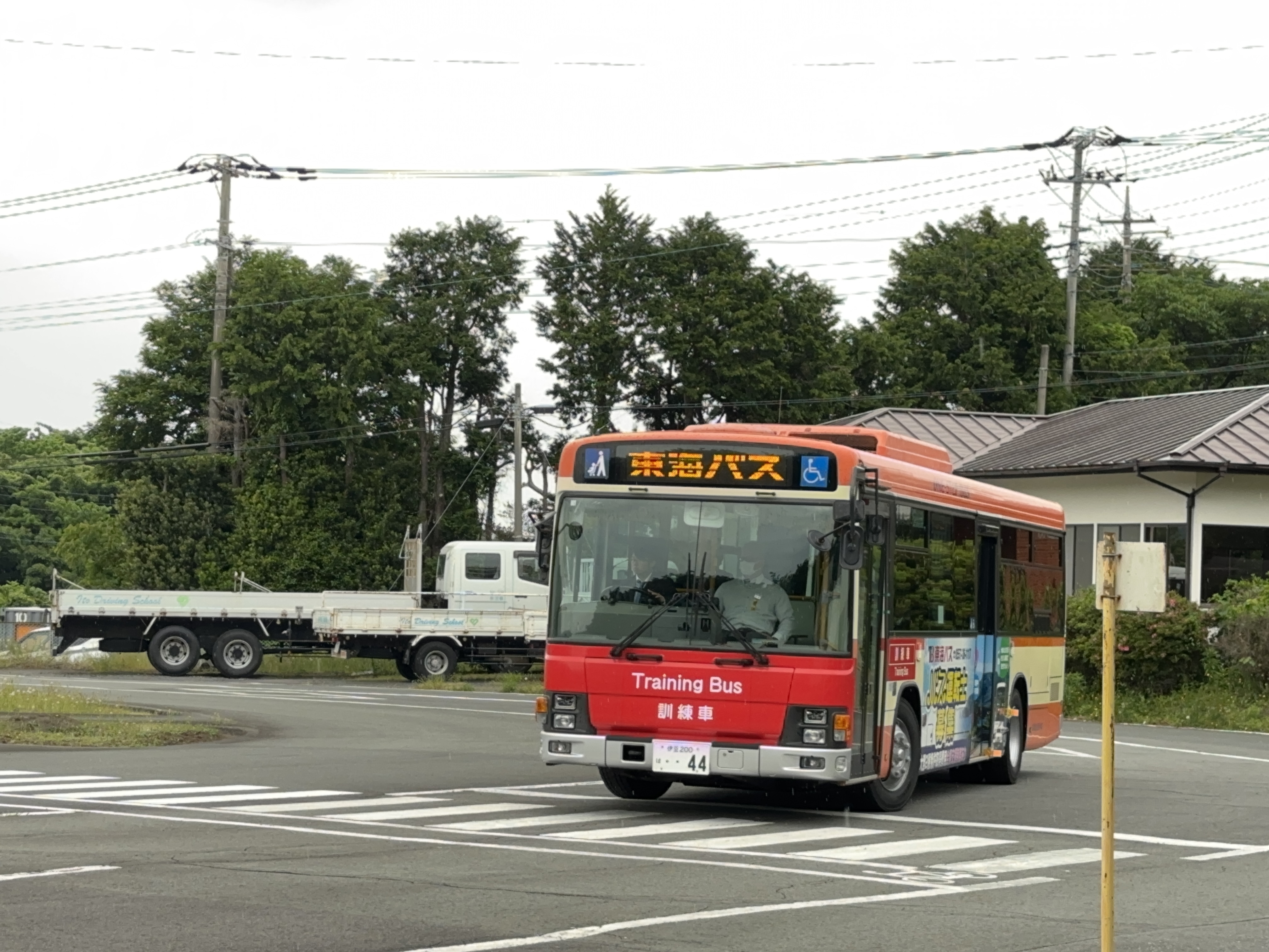 東海バスの運転体験会で、初めてバスの運転席に座り笑顔を見せる30代の参加者。隣にはベテラン運転士が穏やかに見守り、窓の外には緑豊かな伊豆の風景